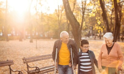 Senior caucasian patient with crutches taking a walk with his wife and grandson in a park